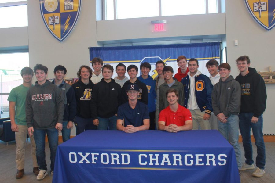 Members of the OHS Baseball team stand and smile around seniors Owen Bruce and Sam Bianco. Bruce and Bianco both signed to further their baseball careers in college.