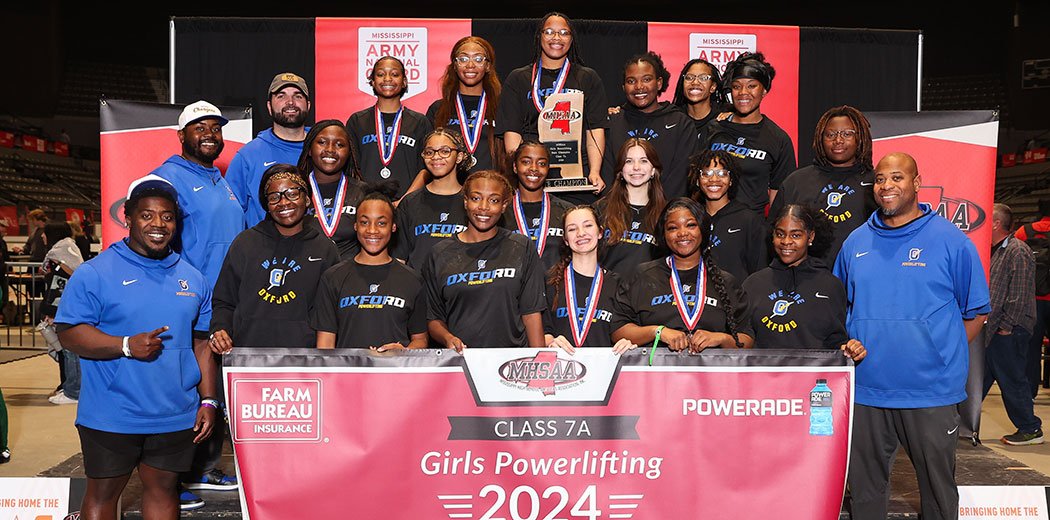The+OHS+Girls+Powerlifting+team+poses+for+a+picture+with+their+2024+7A+state+championship+banner.